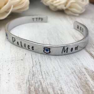 May include: Silver bracelet with the words "Police Mom" and a blue police badge charm.