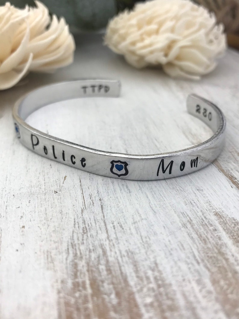May include: Silver bracelet with the words "Police Mom" and a blue police badge charm.