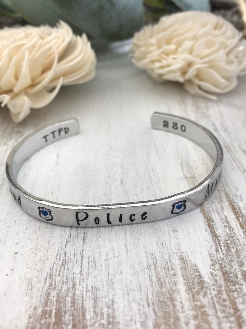 May include: Silver bracelet with the words "TTPD 230" and "Police" engraved on it. The bracelet also has a small blue enamel badge with a heart.