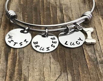 May include: A silver bangle bracelet with three charms that say "WINST", "BRUISER", and "LUCY" and a bone charm.