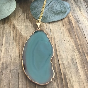 May include: A gold chain necklace with a large, green agate pendant. The pendant is a natural slice of agate with a gold-toned edge.
