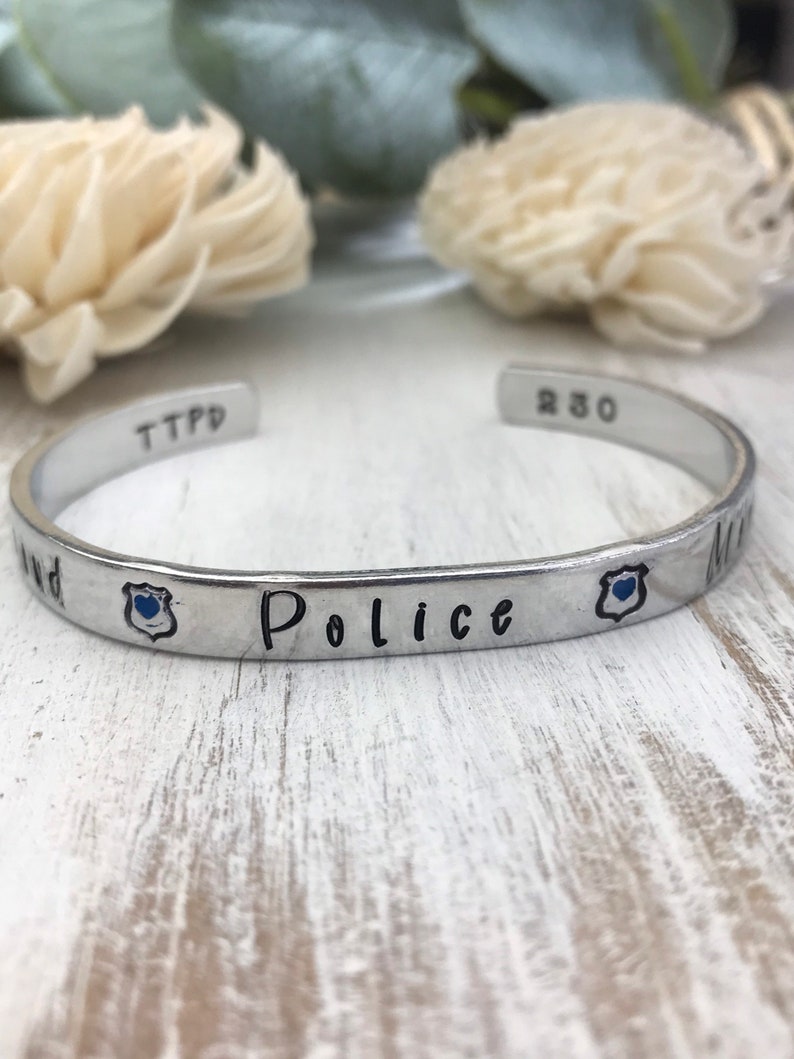 May include: Silver bracelet with the words "Police" and "My" engraved on it. The bracelet also has a small blue badge charm with a heart in the center.