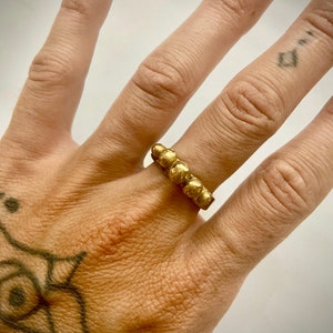 May include: A gold ring with a beaded design. The ring is worn on the ring finger of a hand.