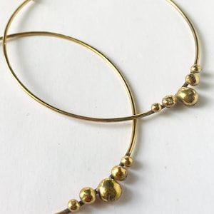 Könnte beinhalten: Goldene Creolen mit einem Cluster kleiner, unregelmäßiger goldener Perlen, die am unteren Ende des Kreises hängen.