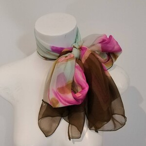 May include: A brown, pink and green patterned silk scarf tied in a bow on a white mannequin.