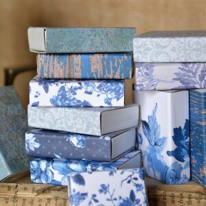 May include: A stack of small, blue and white patterned boxes. The boxes are made of cardboard and have a variety of designs, including floral, geometric, and abstract patterns.
