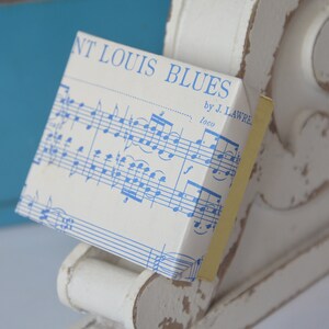 May include: A white box with blue musical notes printed on it. The box has the text "St. Louis Blues by J. Lawre" printed on it.