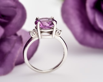 May include: A silver ring with a large, oval-shaped amethyst gemstone and two smaller diamond accents.