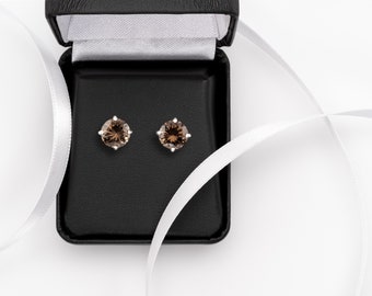 May include: A pair of brown gemstone earrings in a black jewelry box with a white ribbon.