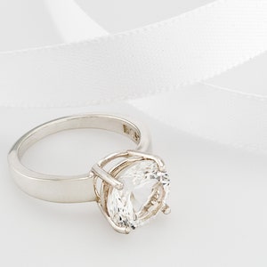 May include: A silver ring with a large, clear, round gemstone set in a cage-like design.