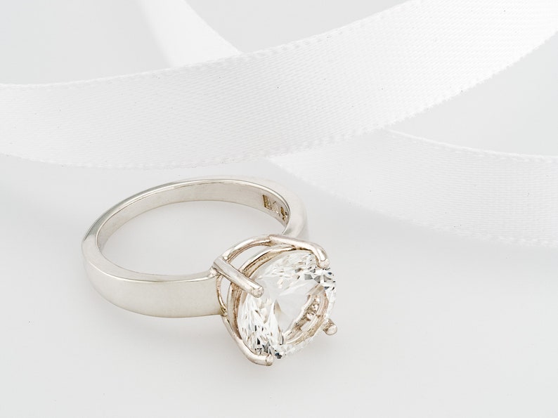 May include: A silver ring with a large, clear, round gemstone set in a cage-like design.