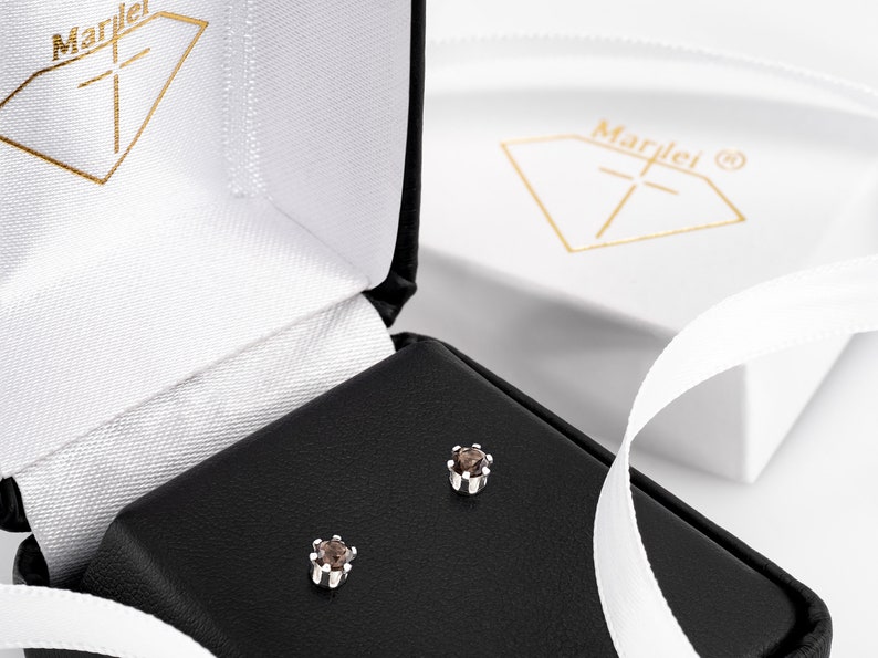 May include: A pair of small, brown gemstone earrings in a black jewellery box. The earrings are set in silver and have a simple, elegant design.