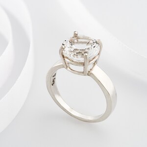 May include: A silver ring with a large, clear, round gemstone set in a cage-like design.