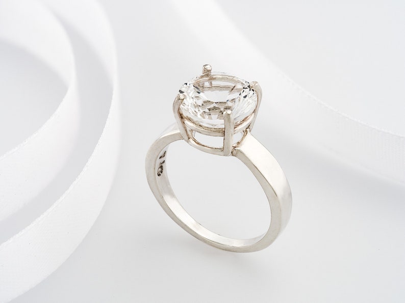 May include: A silver ring with a large, clear, round gemstone set in a cage-like design.