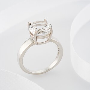 May include: A silver ring with a large, clear, oval-shaped gemstone.