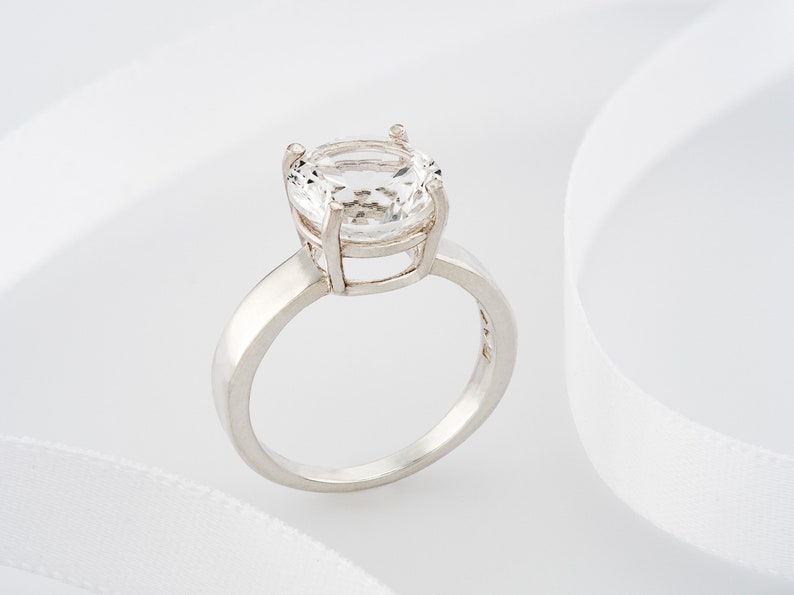 May include: A silver ring with a large, clear, oval-shaped gemstone.