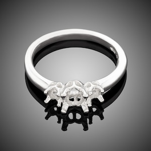 May include: A silver ring with three prongs for setting stones. The ring is on a black background.
