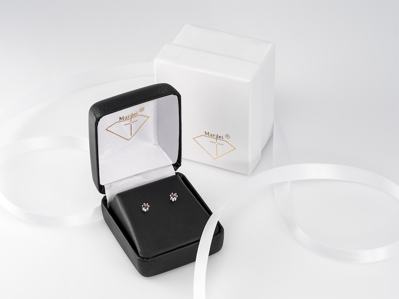 May include: A black jewellery box with a white interior and a small pair of diamond earrings inside. The box is open and the earrings are visible. The box has the word "Mardei" printed on the outside.