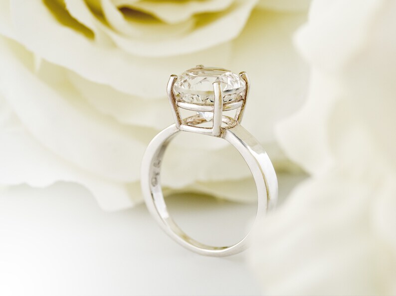 May include: A silver ring with a large, clear, round diamond set in a cage-like setting.
