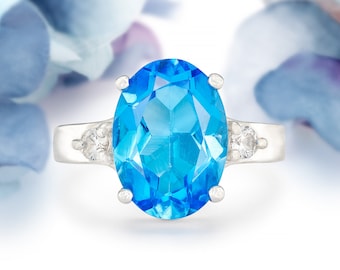May include: A silver ring with a large oval-shaped blue topaz gemstone and two smaller clear gemstones on the band.