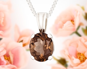 May include: A silver chain necklace with a brown gemstone pendant. The pendant is round and has a faceted cut. The necklace is photographed against a background of pink flowers.