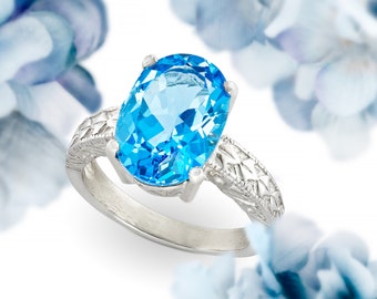 May include: A silver ring with a large oval-shaped blue topaz gemstone. The ring has a delicate, intricate design.