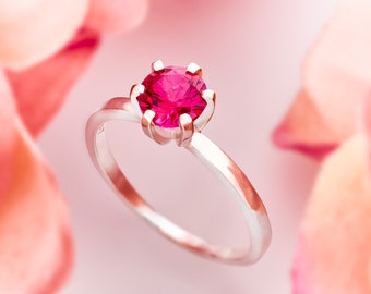 May include: A silver ring with a bright pink gemstone set in a prong setting.