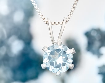 May include: A silver chain necklace with a light blue gemstone pendant. The gemstone is a round cut and has a faceted design.