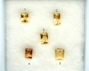 May include: Five rectangular gemstones in shades of yellow and orange are displayed in a white box. Each stone is numbered from 1 to 5. The gemstones vary slightly in color and clarity, with a range of golden hues.