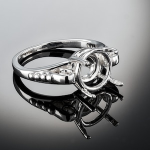 May include: A silver ring setting with a round center stone setting. The ring has a beaded band and a delicate design.