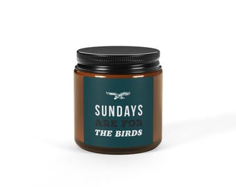 Può includere: Un barattolo di vetro marrone per candele con un coperchio nero e un'etichetta verde acqua che recita "Sundays Are For The Birds".