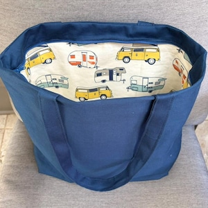 May include: A solid navy blue tote bag with two matching handles and a zippered top closure. The interior lining is an off-white fabric featuring a repeating pattern of yellow camper vans and vintage-style travel trailers in shades of teal and gray.