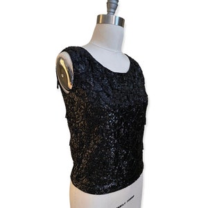 May include: A black sleeveless top with a sequined design. The top is fitted and has a scoop neckline.