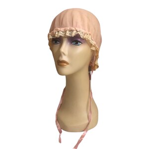 May include: A pink fabric bonnet with a lace trim and matching pink ribbon ties. The bonnet is on a mannequin head.