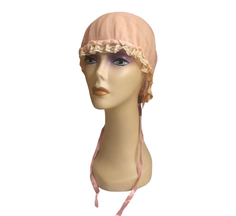 May include: A pink fabric bonnet with a lace trim and matching pink ribbon ties. The bonnet is on a mannequin head.