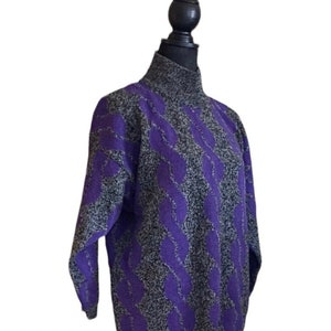May include: A purple and gray cable knit sweater with a turtleneck. The sweater has a textured pattern of purple cables against a gray background. The long-sleeved sweater is displayed on a black mannequin.