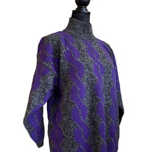 May include: A gray and purple sweater with a high neck and a cable knit design. The sweater is displayed on a black mannequin. The cable knit pattern is a vibrant purple color, and the rest of the sweater is a speckled gray.