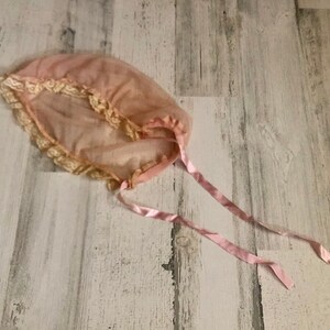May include: A pink sheer baby bonnet with lace trim and pink satin ribbons.