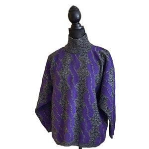 May include: A gray and purple cable knit sweater with a turtleneck. The sweater features a repeating pattern of purple cable knit designs against a gray background. The sweater is displayed on a black mannequin.