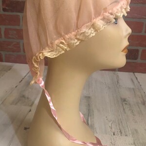May include: A pink mesh shower cap with a lace trim and a pink satin ribbon tie.