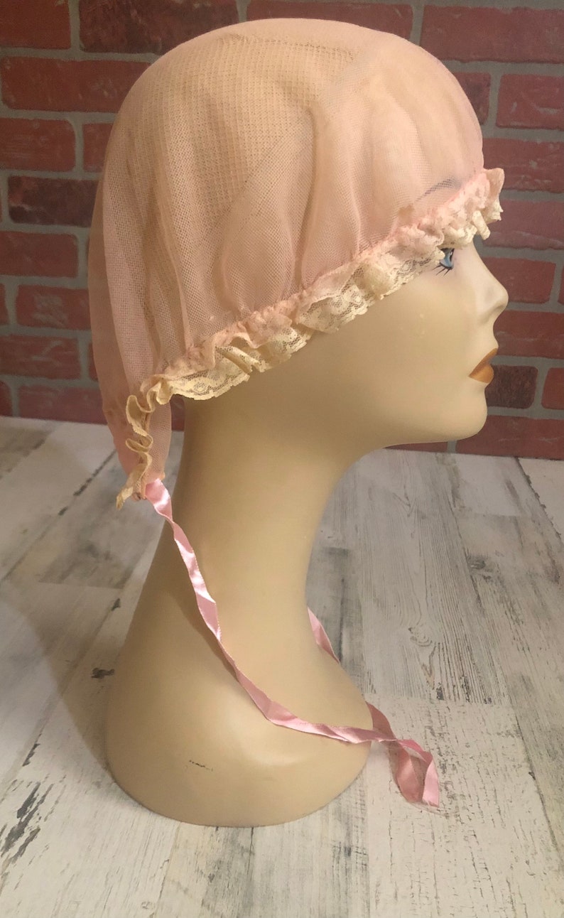 May include: A pink mesh shower cap with a lace trim and a pink satin ribbon tie.