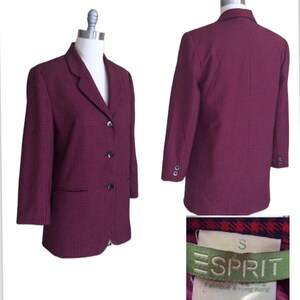 May include: A red and black checkered blazer with a single-breasted closure and three buttons. The blazer has a small pocket on the left side and is labeled "ESPRIT" in green with the size "S" in white. The label also says "Fabriqu&eacute; &agrave; Hong Kong".