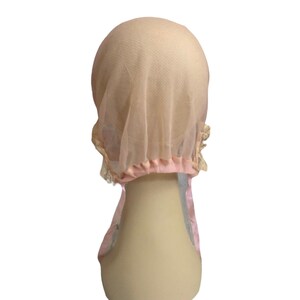 May include: A pink mesh hair net with a lace trim. The net is gathered at the top and has a pink elastic band.