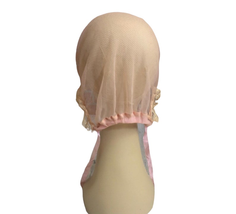 May include: A pink mesh hair net with a lace trim. The net is gathered at the top and has a pink elastic band.