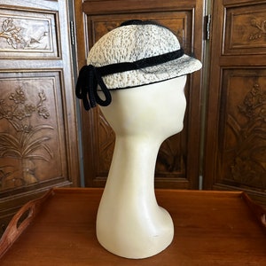 May include: A white and black hat with a black velvet band and a black bow. The hat is on a white mannequin head.