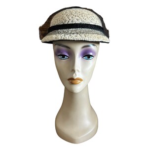 May include: A white and brown woven hat with a black band and a brim. The hat is on a white mannequin head.