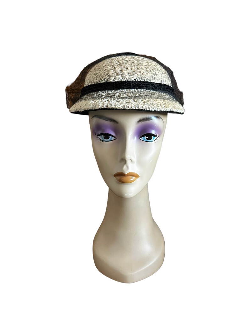 May include: A white and brown woven hat with a black band and a brim. The hat is on a white mannequin head.
