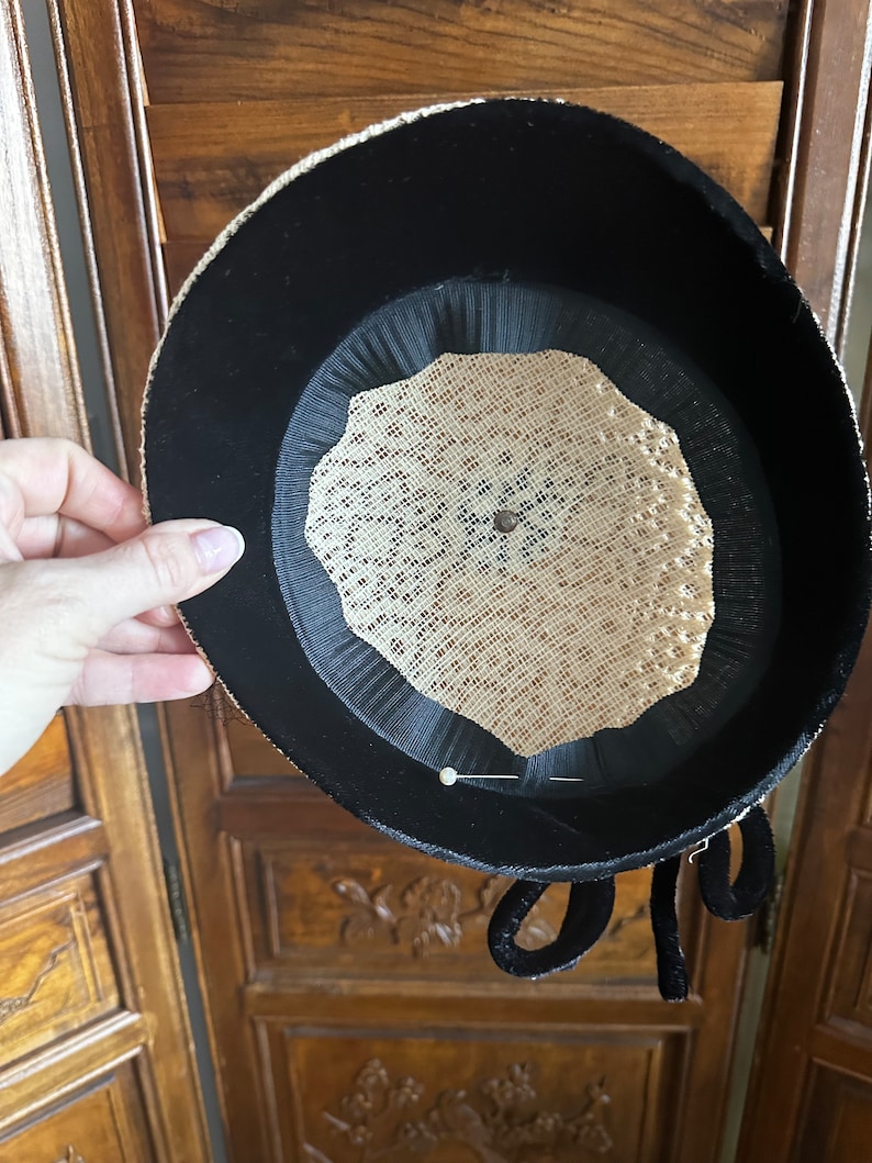 May include: Black velvet hat with a beige mesh lining and a black velvet bow. The hat has a pin in the center.