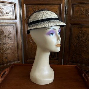 May include: A white straw hat with a black ribbon and black netting. The hat is on a mannequin head.