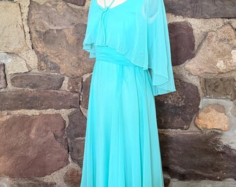 May include: A floor-length turquoise dress featuring a sheer, layered capelet bodice with a V-neckline and thin straps. The garment has a fitted waistline and a flowing, floor-length skirt made of lightweight, semi-sheer fabric over an opaque lining.